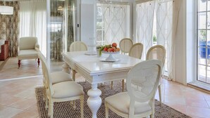 A dining area with a white table, six chairs, a chandelier, and a fruit centerpiece. - Villa Costa Rica - Four Bedroom Villa, Sleeps 8 (Algarve)