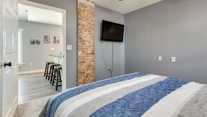 Ein Schlafzimmer mit Bett, einer Wand aus Ziegelsteinen, einem an der Wand befestigten Fernseher und einer Tür zu einem Flur mit Barbereich.