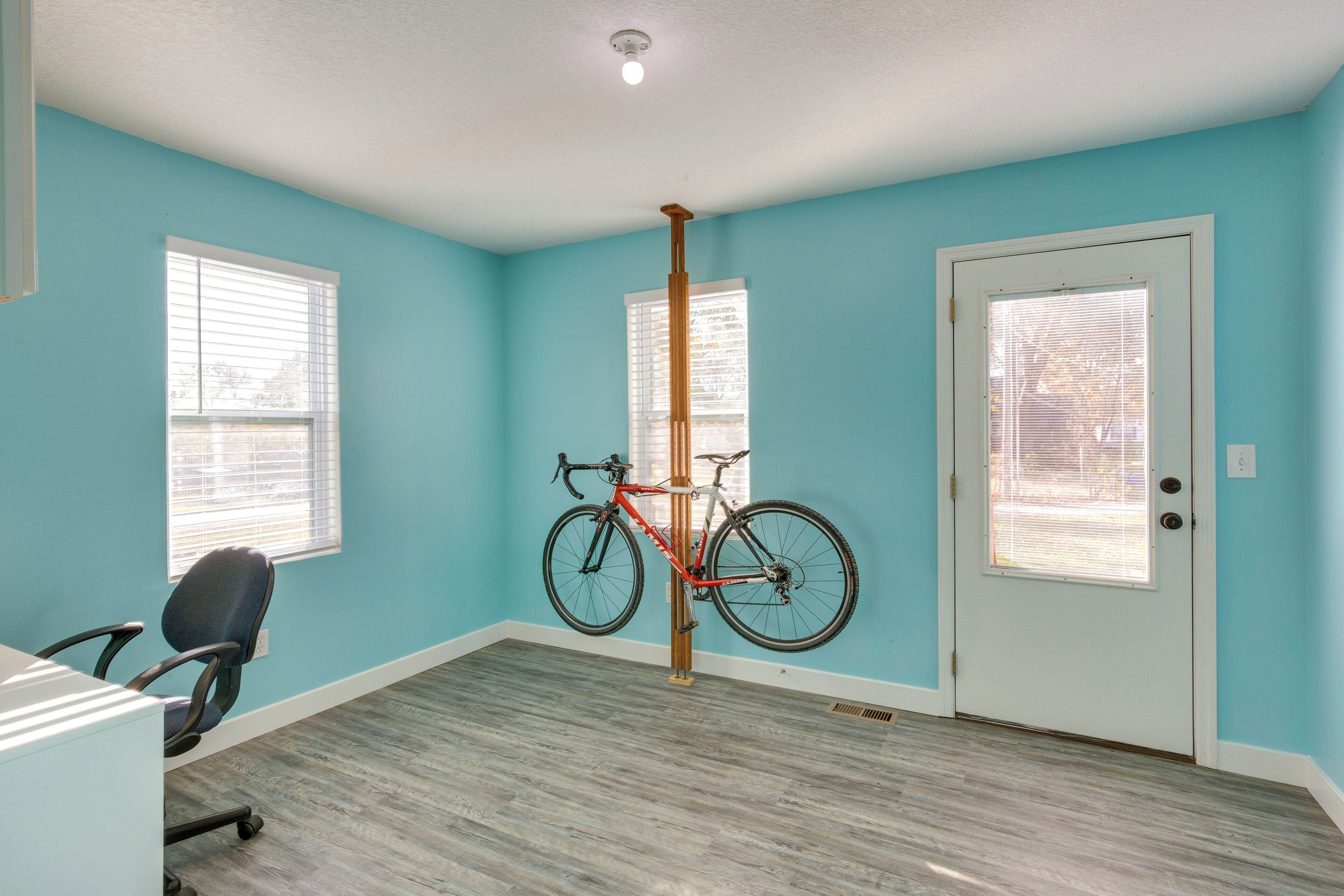 A room with teal walls, a wooden floor, a door, and a bicycle hanging on a pole.