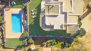 En vy från ovan av en bostadsfastighet med en swimmingpool, en uteplats med sittplatser och en välanlagd trädgård.