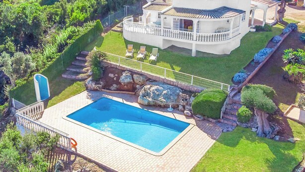 Ett stort hus med en swimmingpool, omgivet av en välskött trädgård och en stenlagd gångväg som leder till poolen.