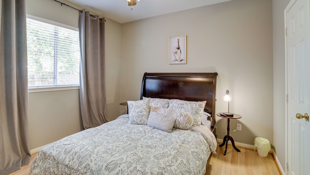 A bedroom with a bed, a ceiling fan, a bedside table with a lamp, a framed picture on the wall, and a door. - Humble Home w/ Game Room, Near Deerbrook Mall! (Kingwood)