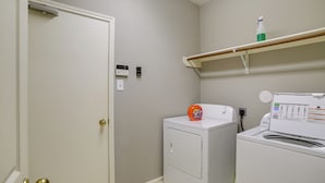 A laundry room with a washing machine, dryer, and a shelf with a spray bottle. - Humble Home w/ Game Room, Near Deerbrook Mall! (Kingwood)