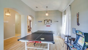 A ping pong table in a room with a chandelier, a gaming chair, and wall art. - Humble Home w/ Game Room, Near Deerbrook Mall! (Kingwood)