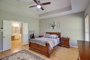 Quarto com cama de madeira, mesa de cabeceira, cômoda, ventoinha no teto e uma janela grande com persianas.