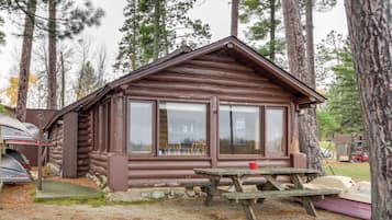 A rustic cabin with a large window, a picnic table, and a canoe nearby.