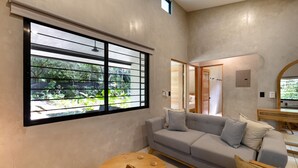 A modern living room with a large window, a grey sofa, a round wooden table, and a mirror on the wall. - Brand New Two bedroom home 5 minutes drive to the surf beaches of Nosara (Playa Pelada)