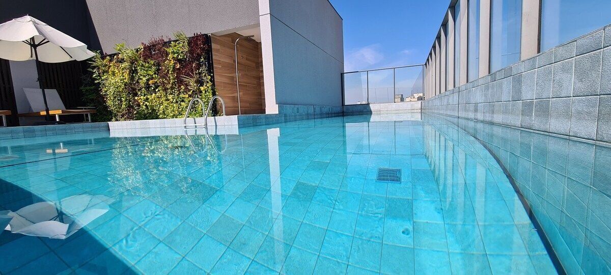 A modern outdoor swimming pool with clear blue water, surrounded by a tiled deck and a low wall.