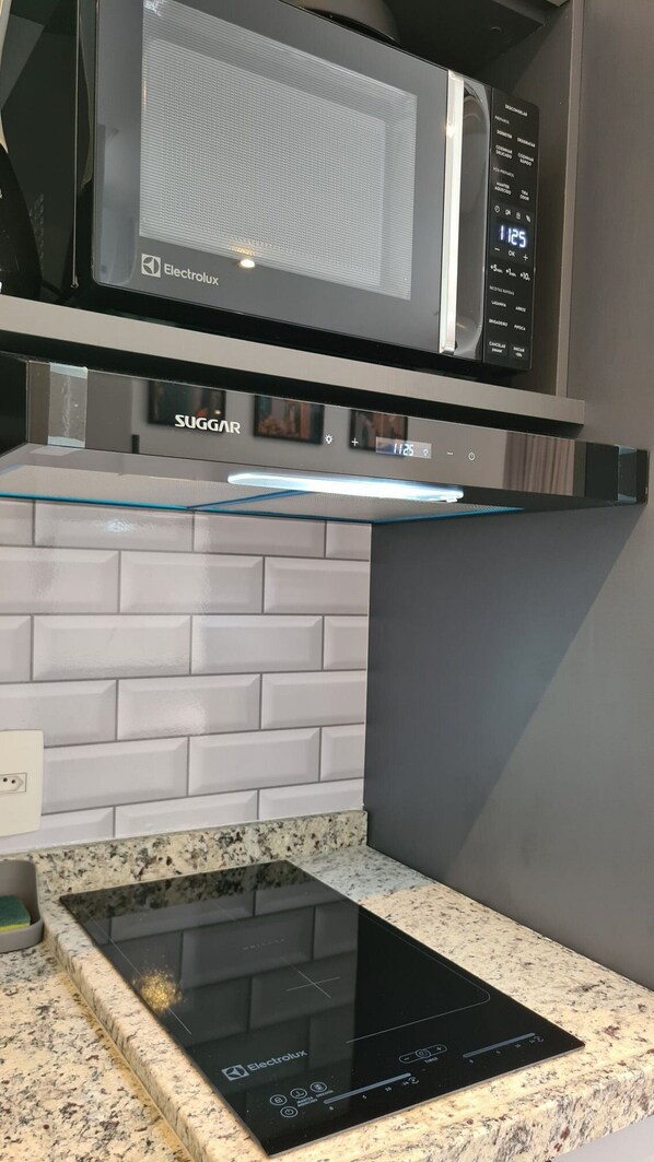 A kitchen with a black induction cooktop, a microwave, and a SUGGAR branded oven.