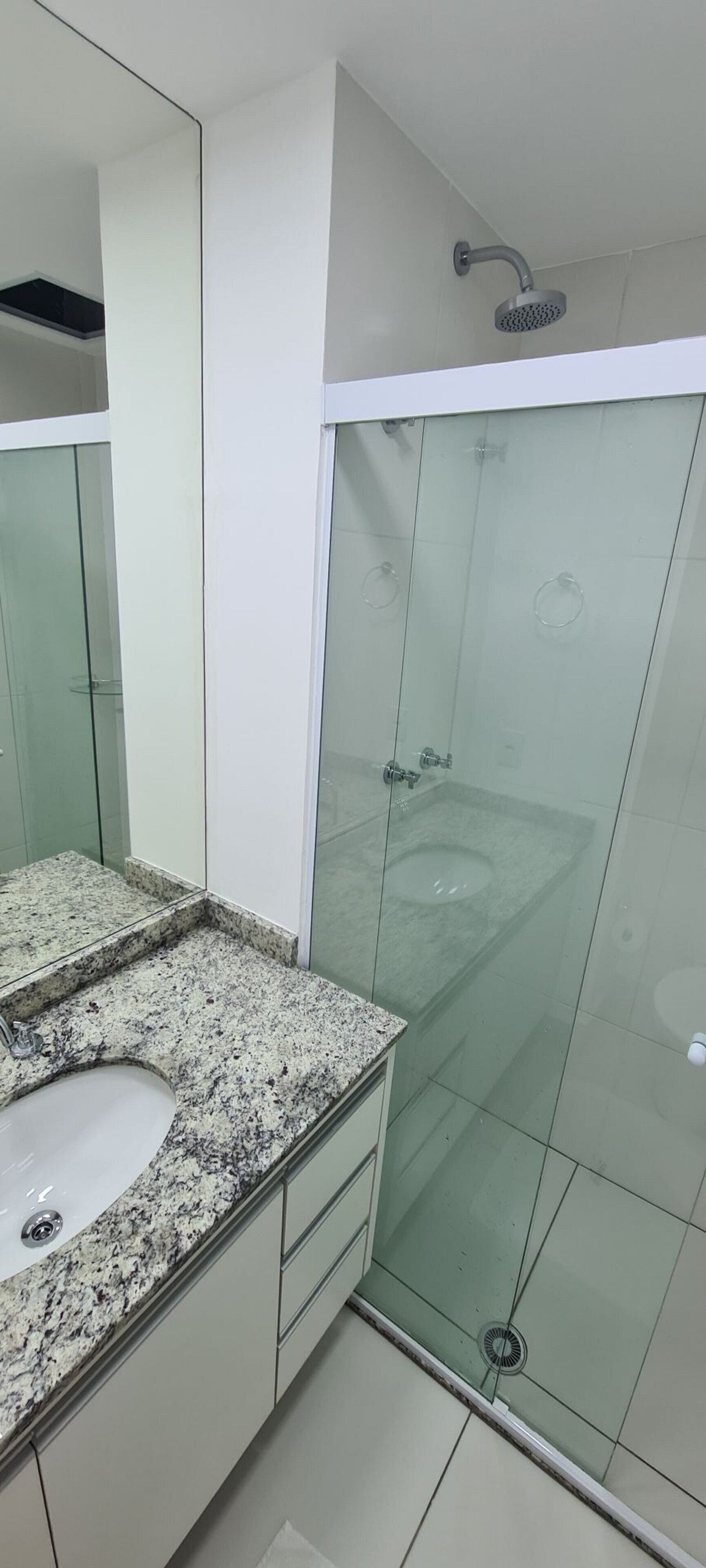A modern bathroom with a granite countertop sink, a glass shower enclosure, and a large mirror.