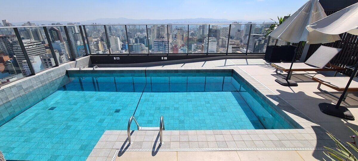 A rooftop swimming pool with clear blue water, surrounded by lounge chairs and umbrellas, offering a city view.