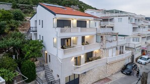Un edificio residencial de varios pisos con balcones, fachada de piedra y vista a la calle con automóviles estacionados.