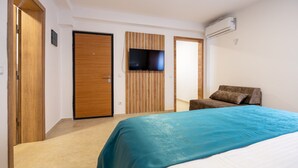 Un dormitorio con cama, televisor montado en la pared, aire acondicionado y una puerta de madera.