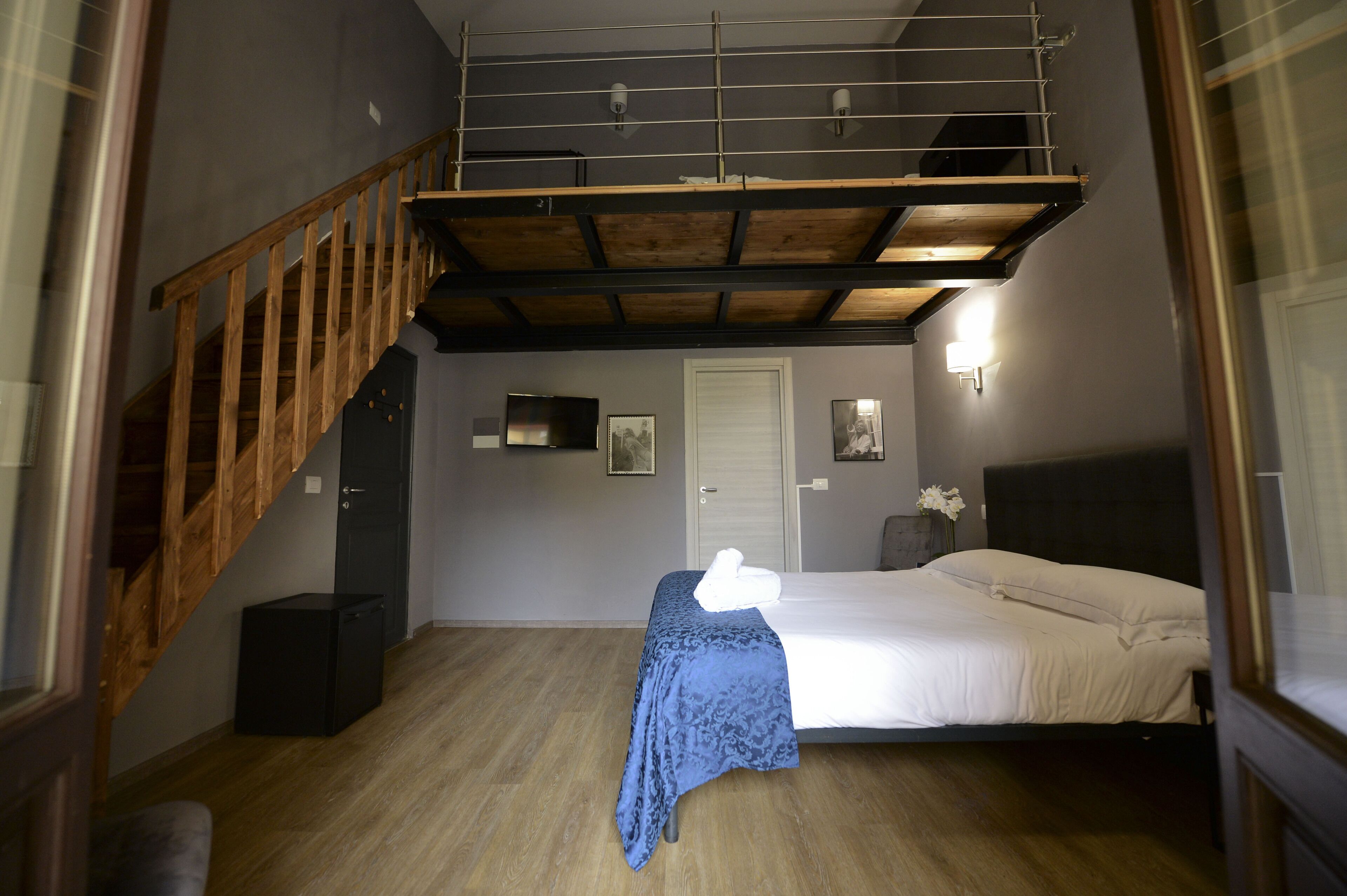Ein Schlafzimmer mit einem Bett, einer Holztreppe, einer Tür und einem kleinen Tisch mit einer Vase.