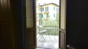 An open door leading to a balcony with a table and chairs, overlooking a building with balconies. - Palazzo Oliveto (Florence)