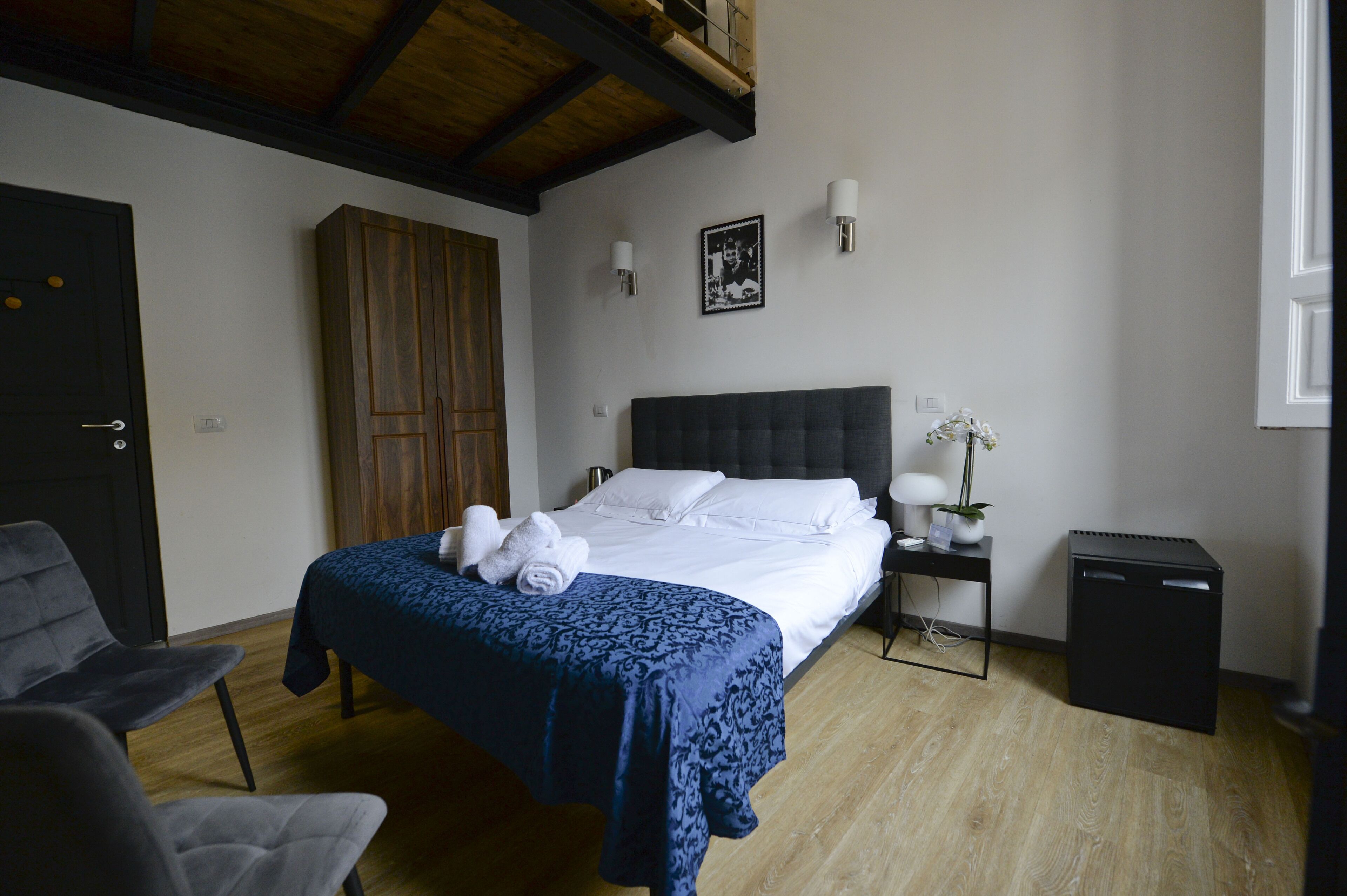 A bedroom with a bed, a desk, a chair, a wardrobe, and a small trash bin.