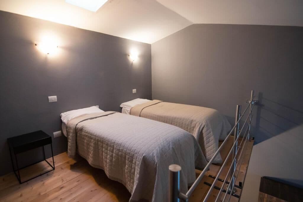 A small, dimly lit room with two beds, a small table, and a staircase.