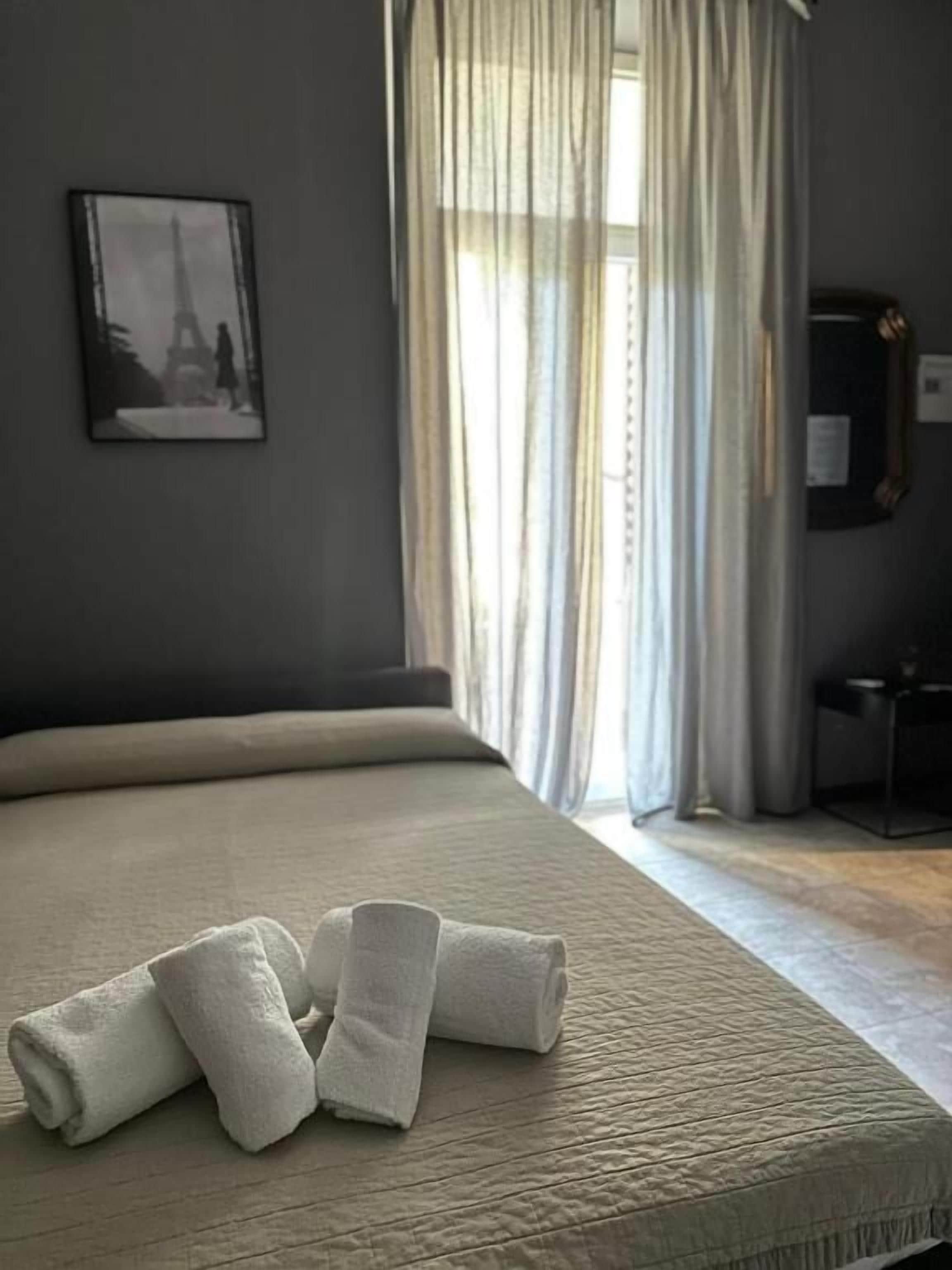 Een hotelkamer met een bed, een raam met gordijnen, een schilderij aan de muur en een klein tafeltje.