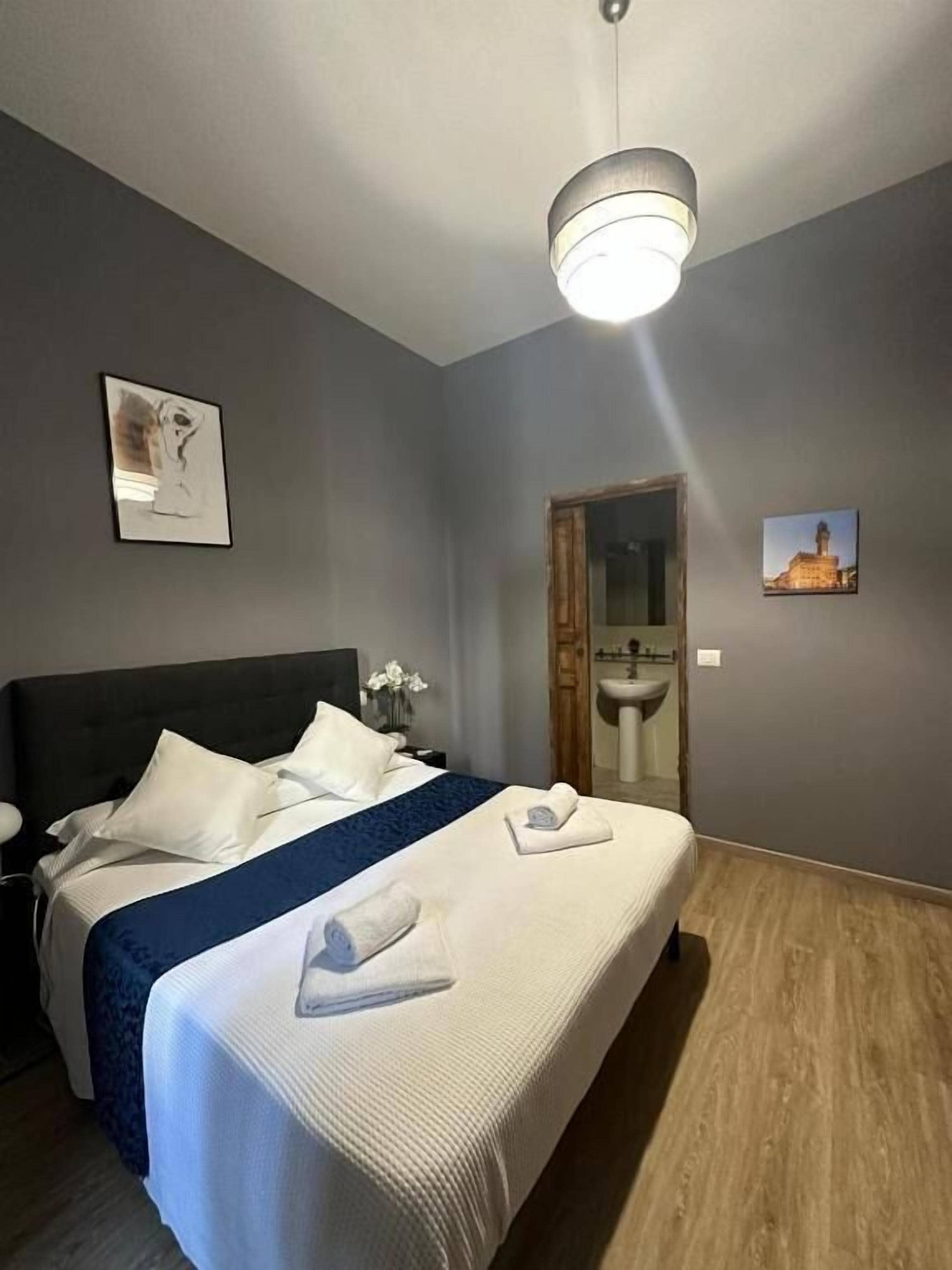 Habitación de hotel con una cama grande, una mesita de noche, una lámpara de pared y una puerta de baño.