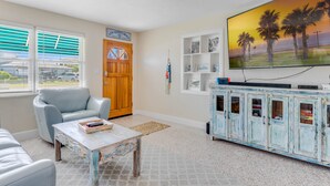 Ein Wohnzimmer mit Fernseher, blauem Sessel, Couchtisch, Holztür und einer Schrank mit Regalen.