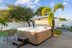 A hot tub with a chair and steps, surrounded by a brick patio, palm trees, and a bicycle. - Book now and save 20% (New Smyrna Beach)
