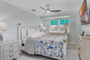 A bedroom with a bed, a nightstand, a dresser, a ceiling fan, a window with blinds, and a TV mounted on the wall. - Book now and save 20% (New Smyrna Beach)