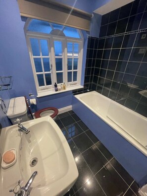 Une salle de bain avec un lavabo blanc, une baignoire et une fenêtre avec des stores.