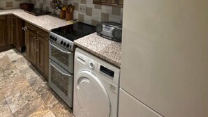 A kitchen with wooden cabinets, a Bosch refrigerator, a stove, a washing machine, and a microwave. - Expansive 4BD Home- 15 min From Buckingham Palace! (London)