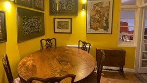 A dining area with a round wooden table surrounded by chairs, yellow walls, and framed artwork on the walls. - Expansive 4BD Home- 15 min From Buckingham Palace! (London)