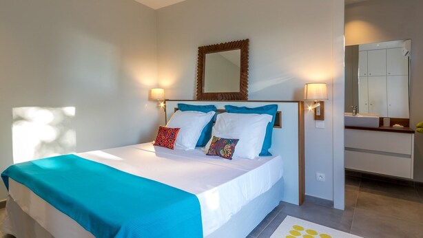 A hotel room with a bed, bedside lamps, a mirror, and a bathroom visible in the background. - Studio-Romantic-Wet room-Sea view-RDC Avec Terrasse privée (La Trinité)