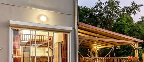 A modern house with a glass door entrance, a wooden deck, and a covered outdoor seating area.