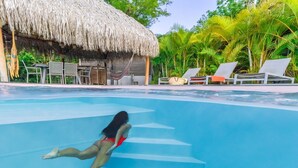 A swimming pool with a person diving, lounge chairs, and a thatched-roof structure. - Studio-Romantic-Wet room-Sea view-RDC Avec Terrasse privée (La Trinité)