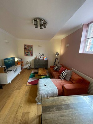 A living room with a sofa, a TV, a coffee table, a lamp, and a wall with a picture. - Chic Victorian Flat in Private Estate - Mile End! (London)