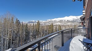 A balcony with a snow-covered ground, overlooking a mountainous landscape with snow-covered trees and mountains.