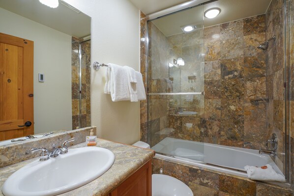 A bathroom with a marble sink, a glass-enclosed shower, and a white toilet.