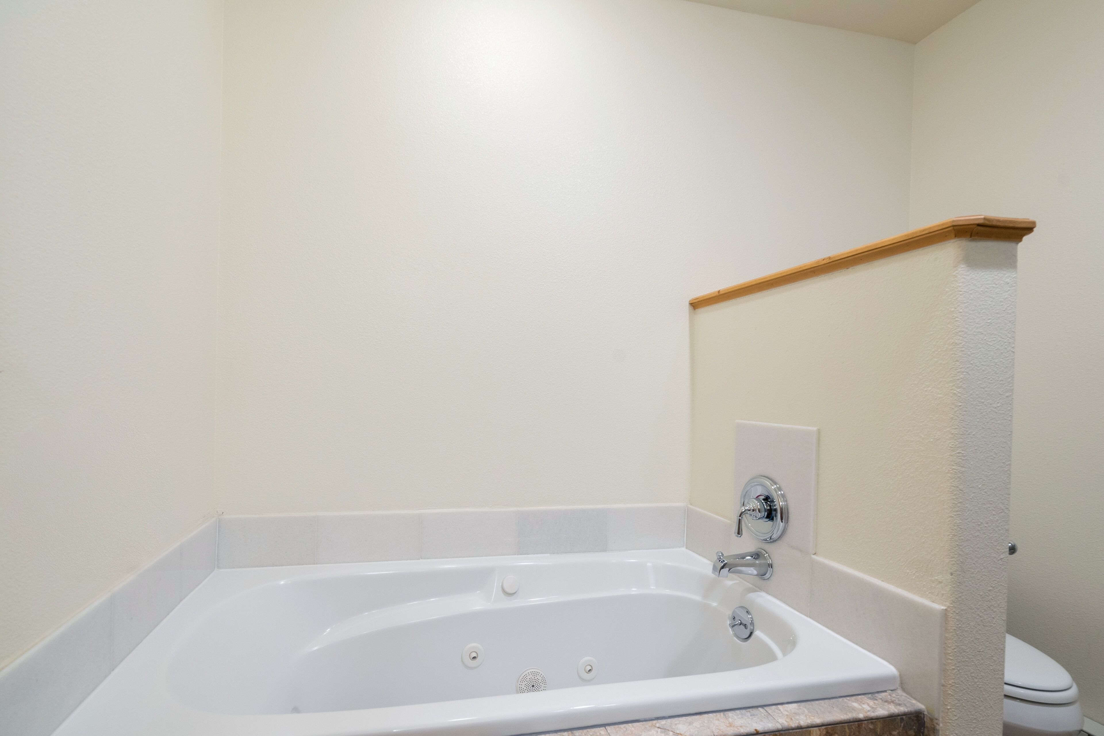 A standard white bathroom with a bathtub, a toilet, and a wooden floorboard.