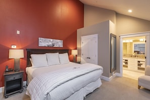 A bedroom with a large bed, a nightstand with a lamp, a painting on the wall, and a closet with a mirror.