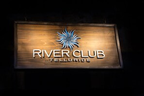 A wooden sign with the text "River Club Telluride" and a stylized sun logo.