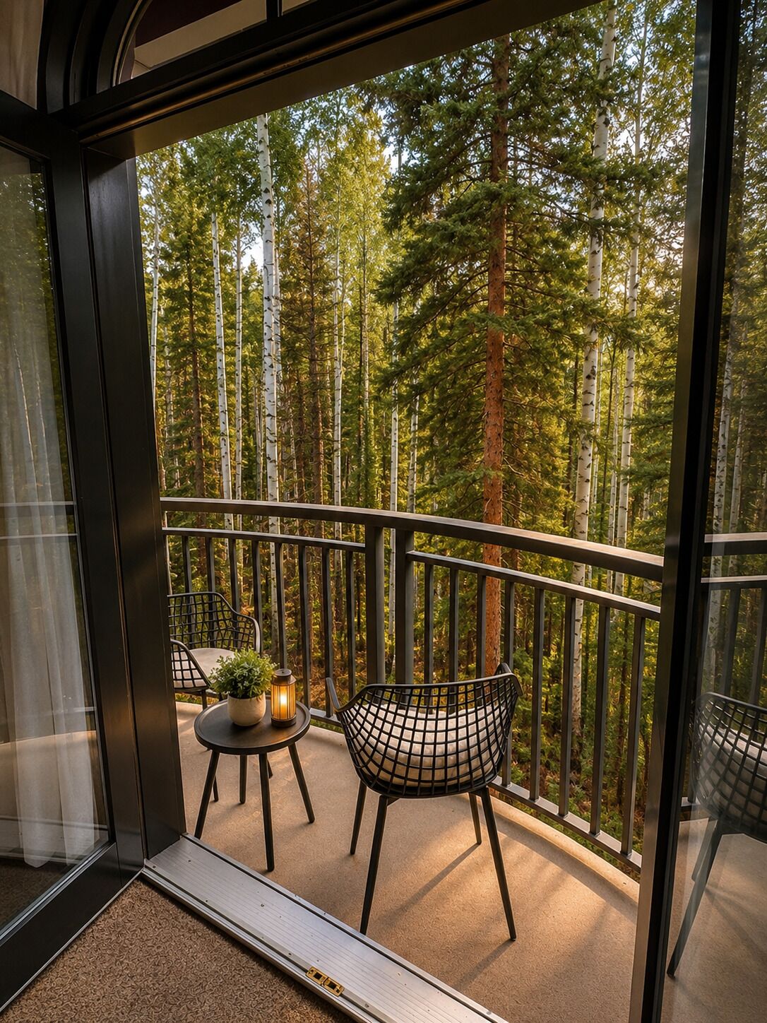 Ein Balkon mit Blick auf einen Wald, ein Tisch mit einer Pflanze und zwei Stühle.