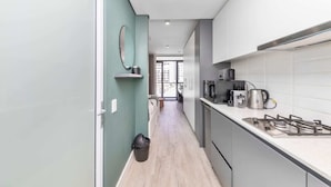 A narrow kitchen with a light-colored floor, a stainless steel stove, and a microwave. - Stunning Studio Apartment With Balcony, Woodstock! (Cape Town)