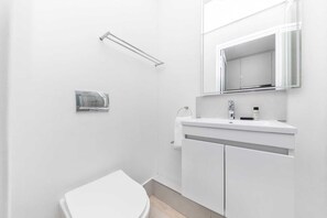 A modern bathroom with a white toilet, a sink with a mirror above it, and a towel rack on the wall. - Stunning Studio Apartment With Balcony, Woodstock! (Cape Town)