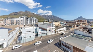 A cityscape with buildings, a road, and mountains in the background. - Stunning Studio Apartment With Balcony, Woodstock! (Cape Town)