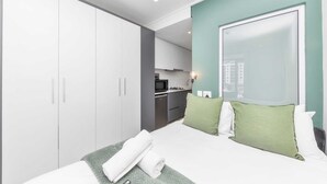 A modern hotel room with a large bed, a wardrobe, a kitchenette, and a view of the city. - Stunning Studio Apartment With Balcony, Woodstock! (Cape Town)