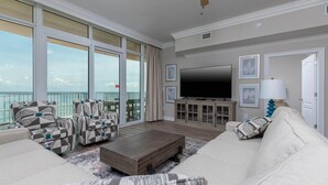 A spacious living room with a large TV, comfortable seating, and a balcony with a view. - Phoenix Orange Beach Ii 905 4 Bedroom Condo (Orange Beach)