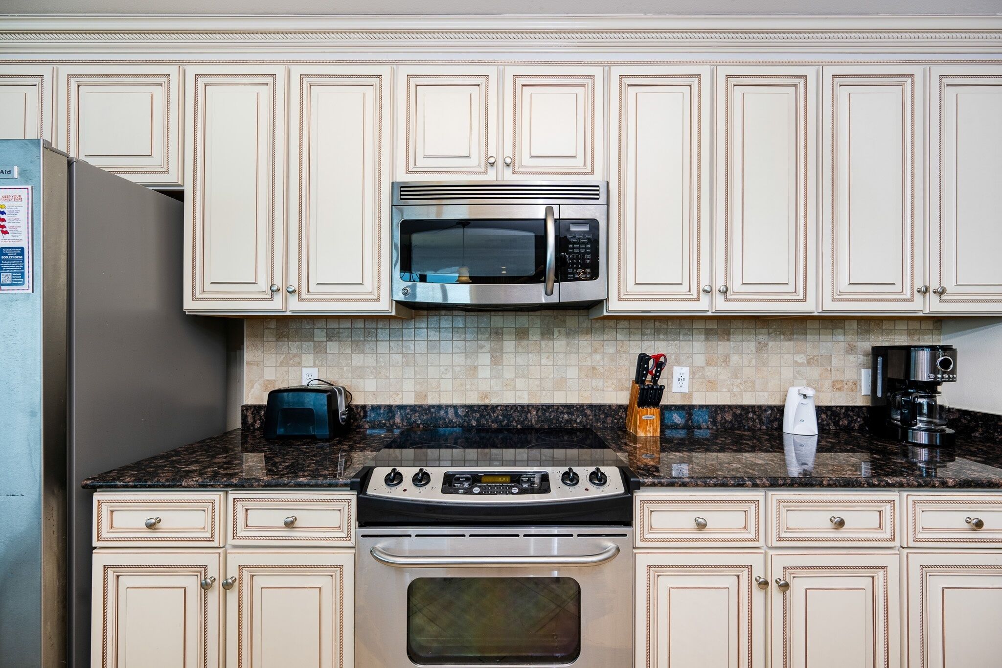 A kitchen with beige cabinets, a stainless steel microwave, a gas stove, and a coffee maker.