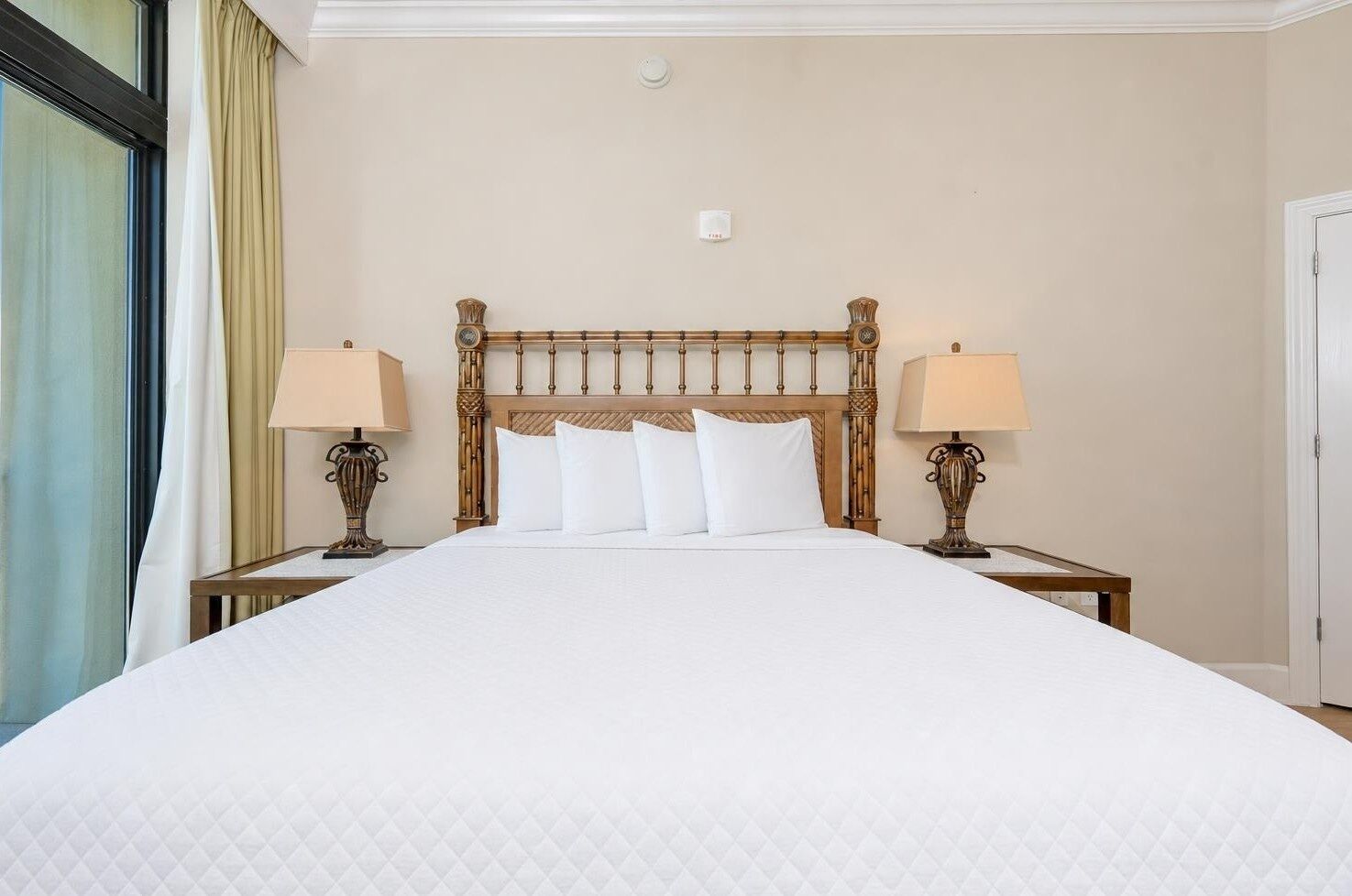 Een hotelkamer met een groot bed, twee nachtkastjes met lampen, een houten hoofdbord en een raam met gordijnen.