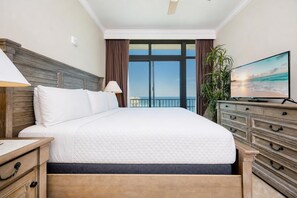 A hotel room with a bed, a TV, a dresser, and a view of the ocean.
