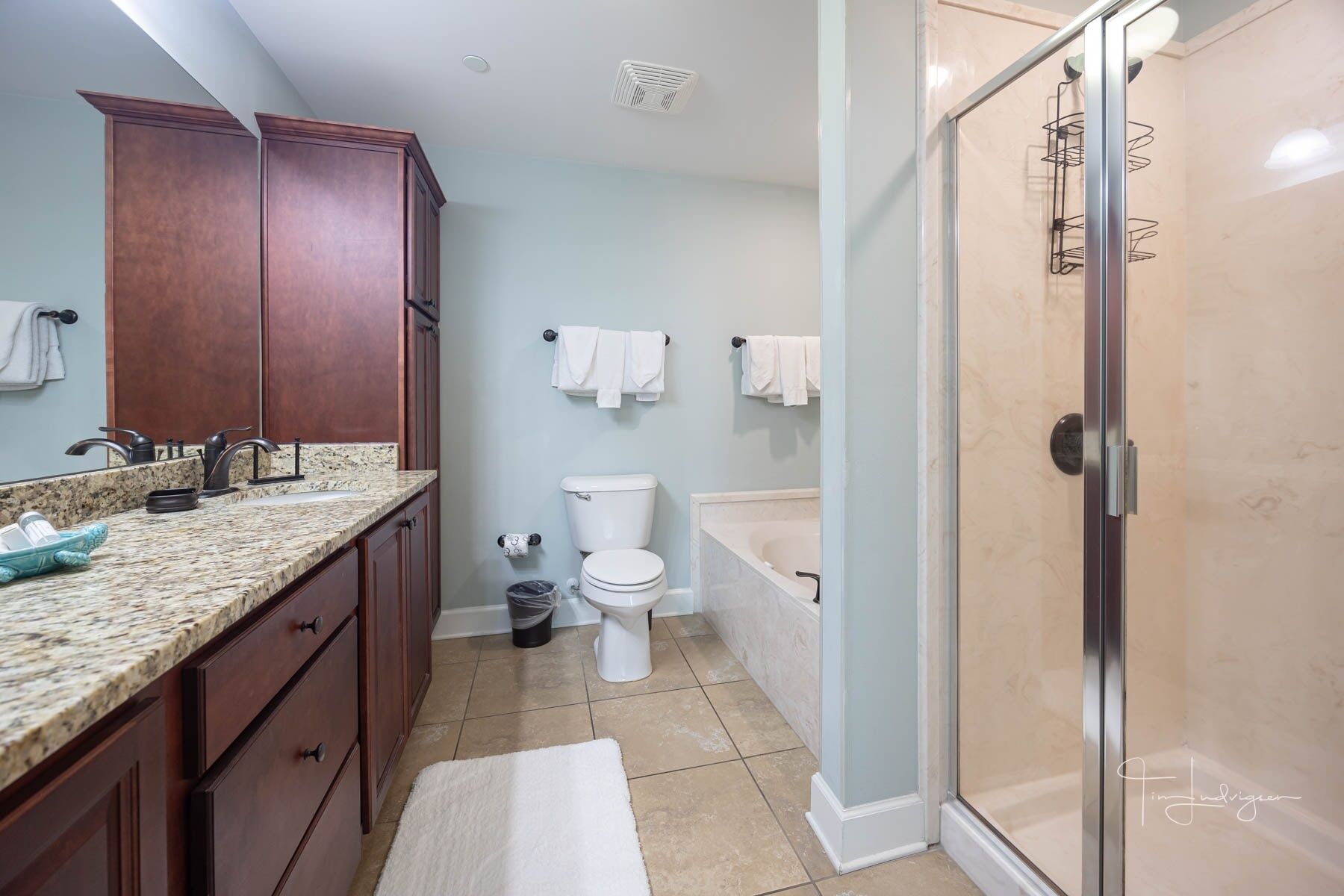 A bathroom with a granite countertop, a toilet, a bathtub, and a shower area.