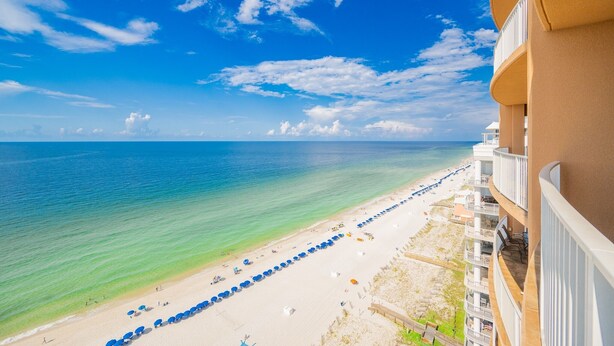 A beach view with a clear sky, a sandy beach, and a building with balconies overlooking the ocean. - Phoenix Gulf Shores 1602-2 2 Bedroom Condo (Gulf Shores)