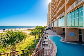 A hotel with a pool, beach view, and a clear sky.